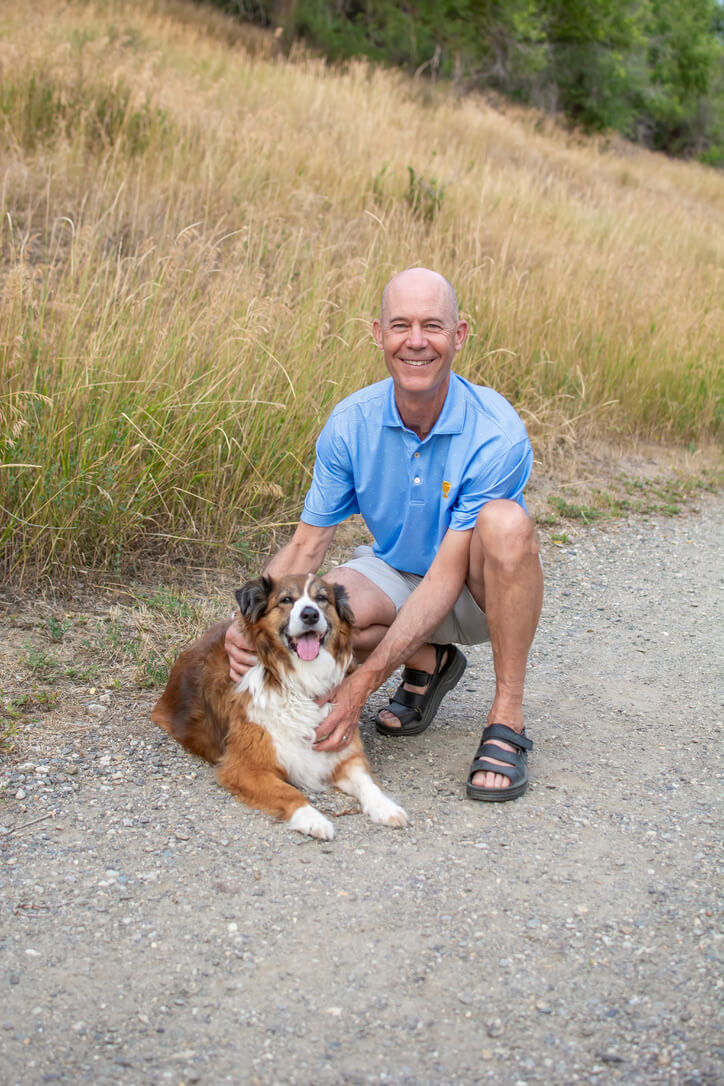 Warren Macdougall crouching on a gravel trail beside a dog