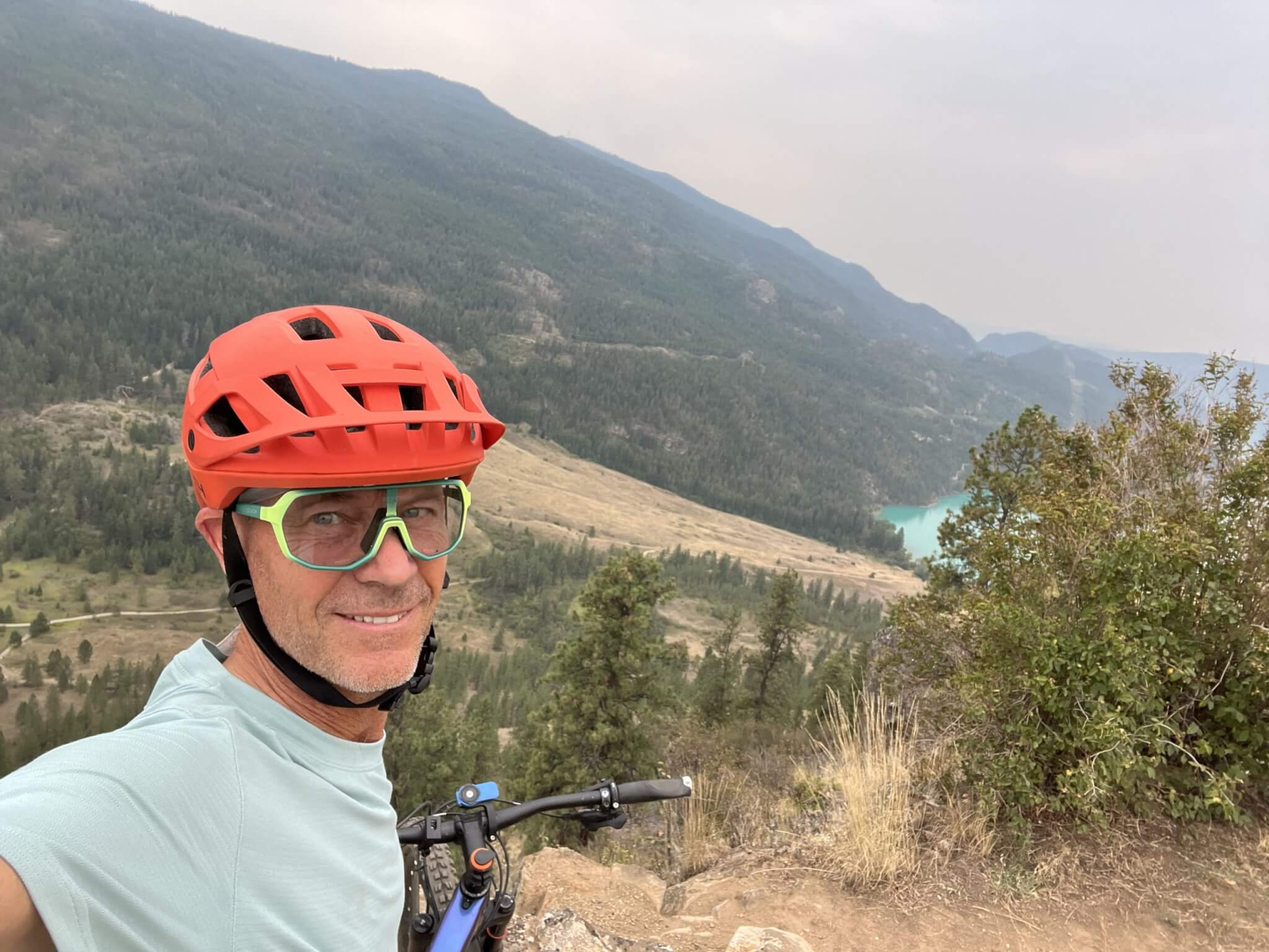 Warren Macdougall in an orange mountain bike helmet on a trail above a lake